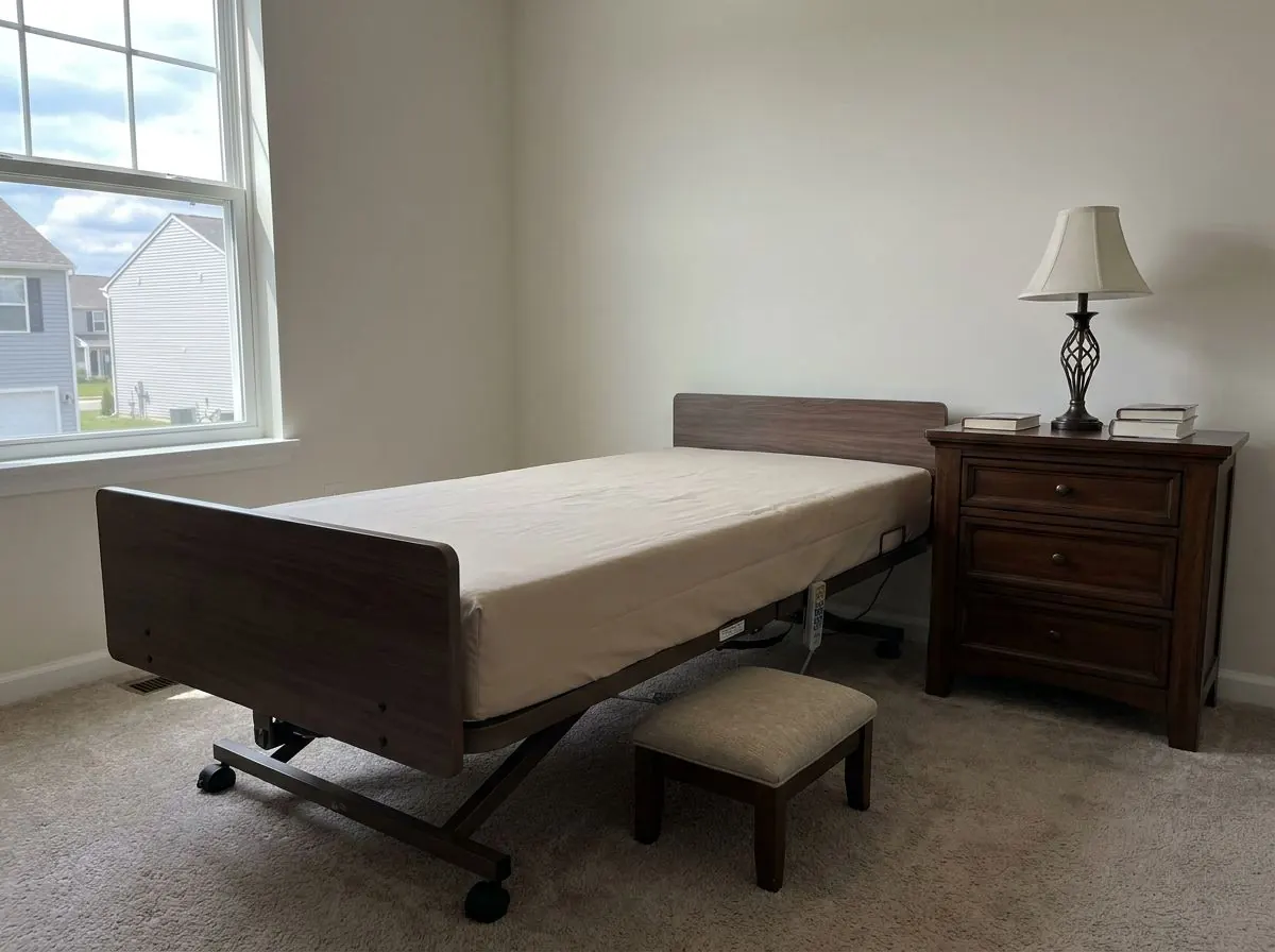 Side view of a hospital bed at its lowest setting, its mattress sitting far below the top of the wooden nightstand beside it.